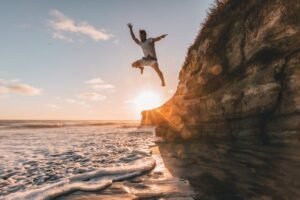 Un homme fait un saut incroyable d'un versant sur la plage, au bord de l'eau.