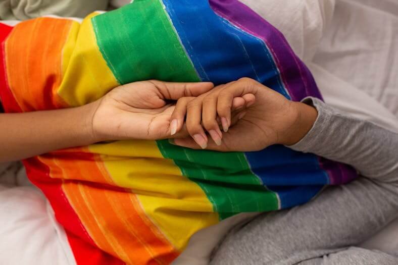 deux femmes se tiennent la main au dessus d'un drapeau lgbt