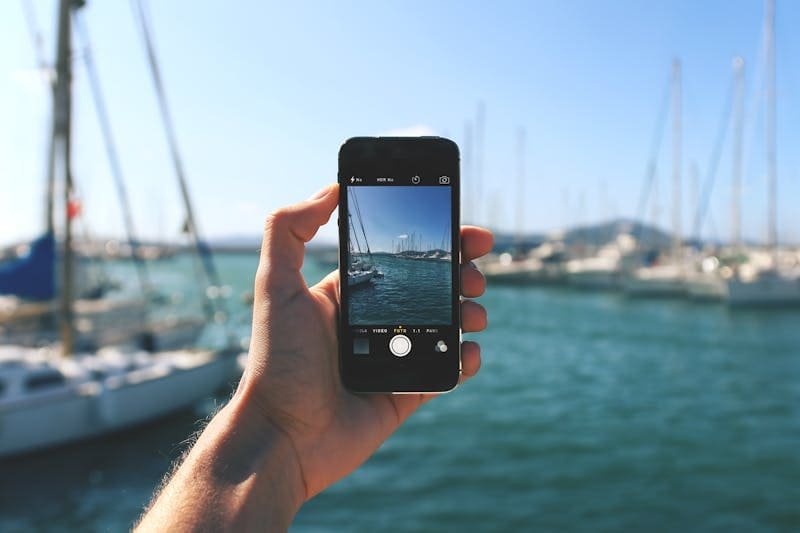 Une main tient un téléphone portable, qui prend une photo de bateaux dans le port à Sal.
